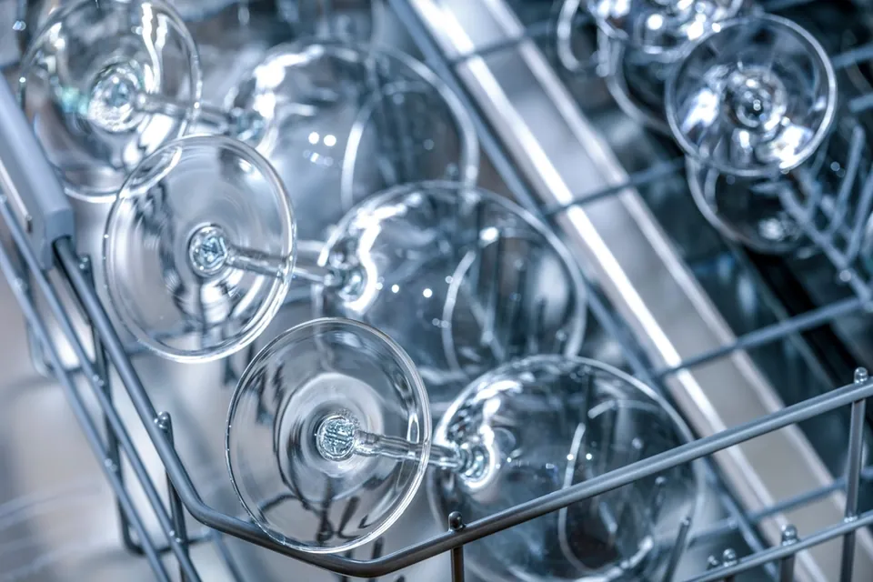 Clean glasses and cutlery in the rack of an open dishwasher