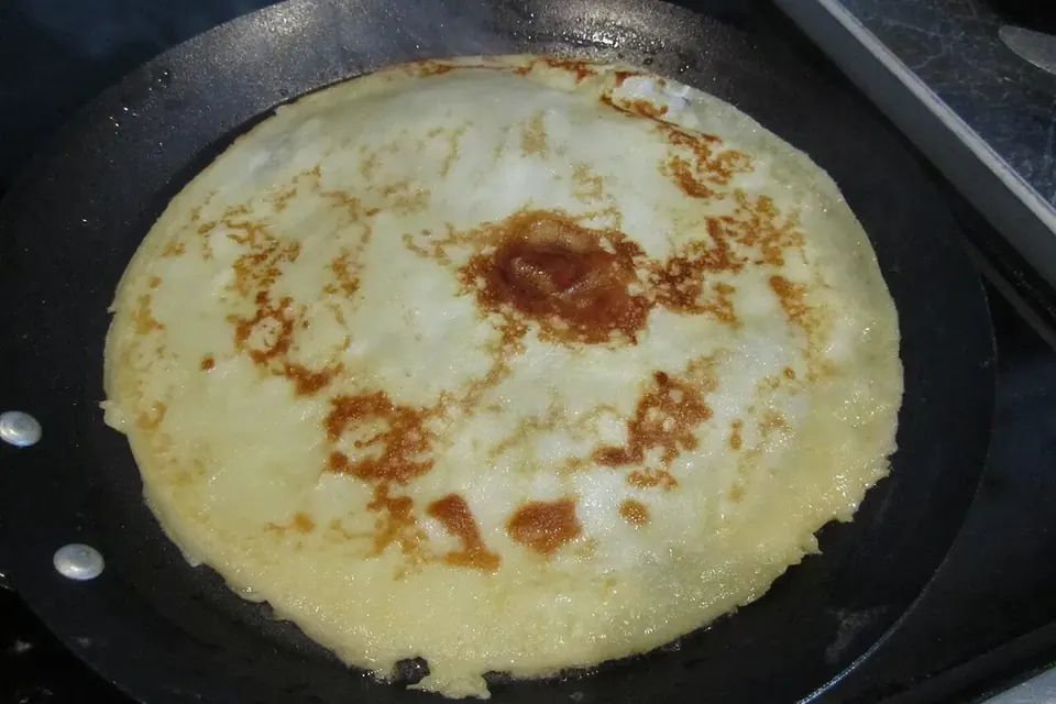 A thin golden crepe cooking in a wide, shallow round pan