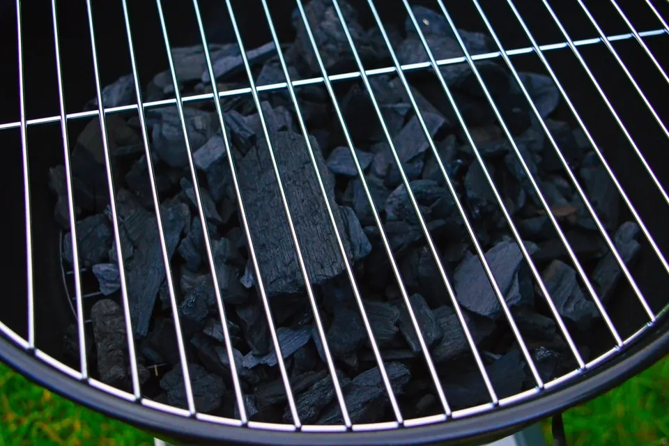 Irregular pieces of black lump charcoal under the cooking grate of a round kettle grill