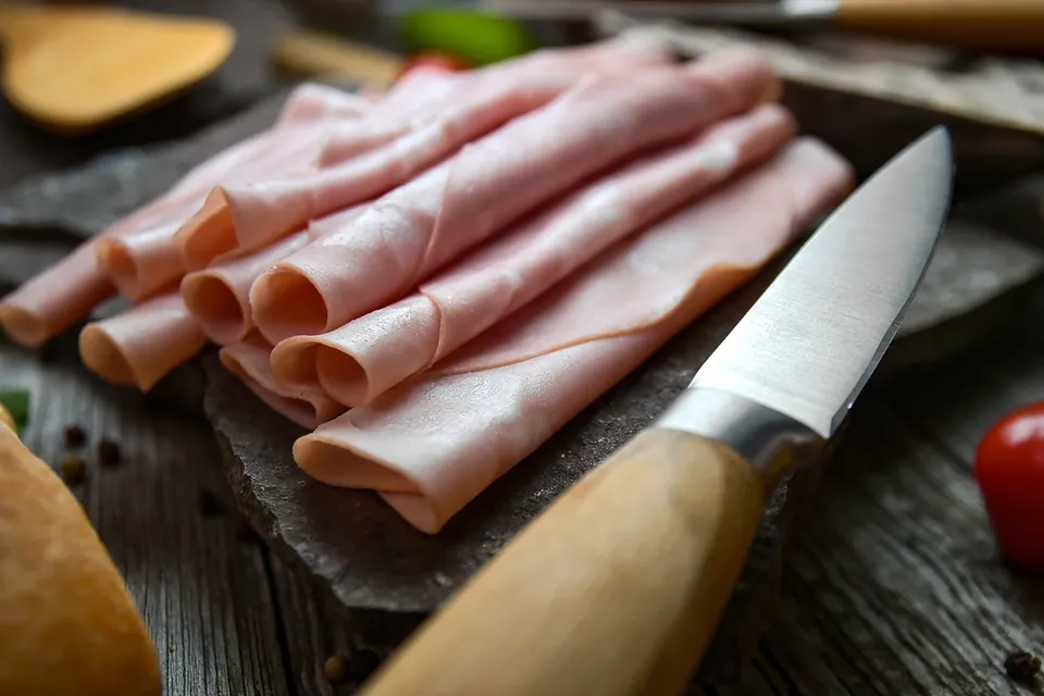Rolled slices of cooked ham beside a small knife on a wooden board