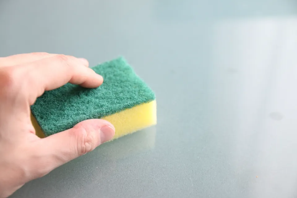 A hand holding a green and yellow scrubbing sponge over a pale counter