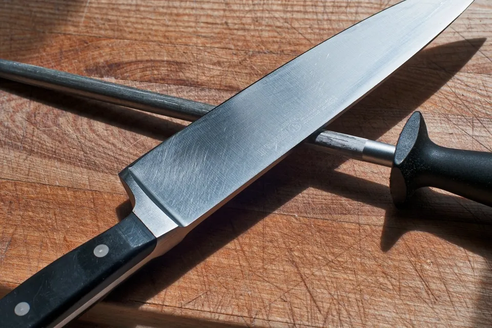 A chef's knife lying across a honing steel on a wooden board