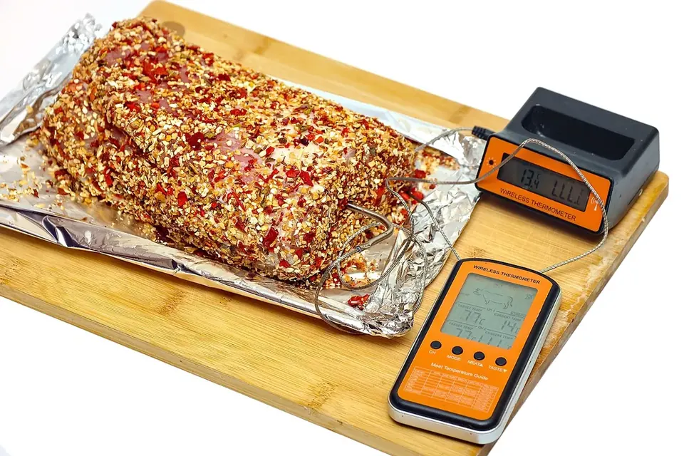 A wireless probe thermometer with two display units beside a seasoned pork joint on a board