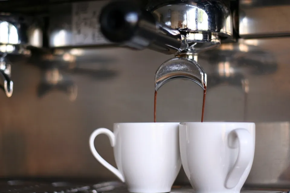 Coffee pouring from a machine's spouts into two white cups